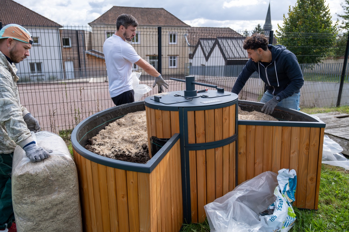 Trois techniciens garnissent la jardinière d’un jardin composteur, devant une école